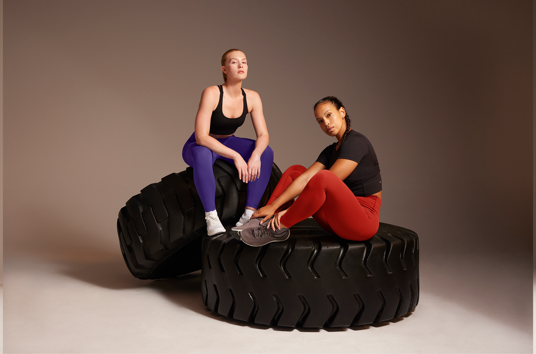 lululemon — two models in purple and red leggings with large tractor tires, neutral taupe studio